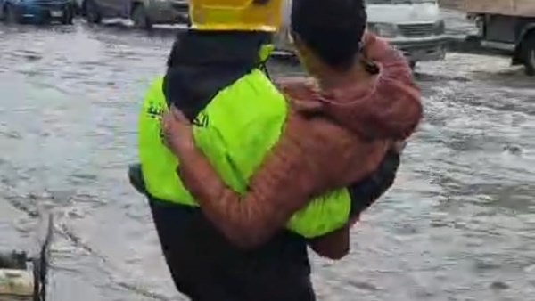 رجل الحماية المدنية يساعد طفلًا على عبور شارع حلوان وسط تراكمات مياه الأمطار 